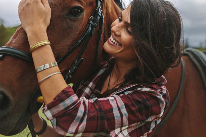 A woman in a plad shirt petting a brown horse